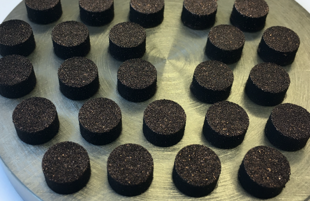 Dark coloured graphene coated copper tablets on a metal scale during testing.